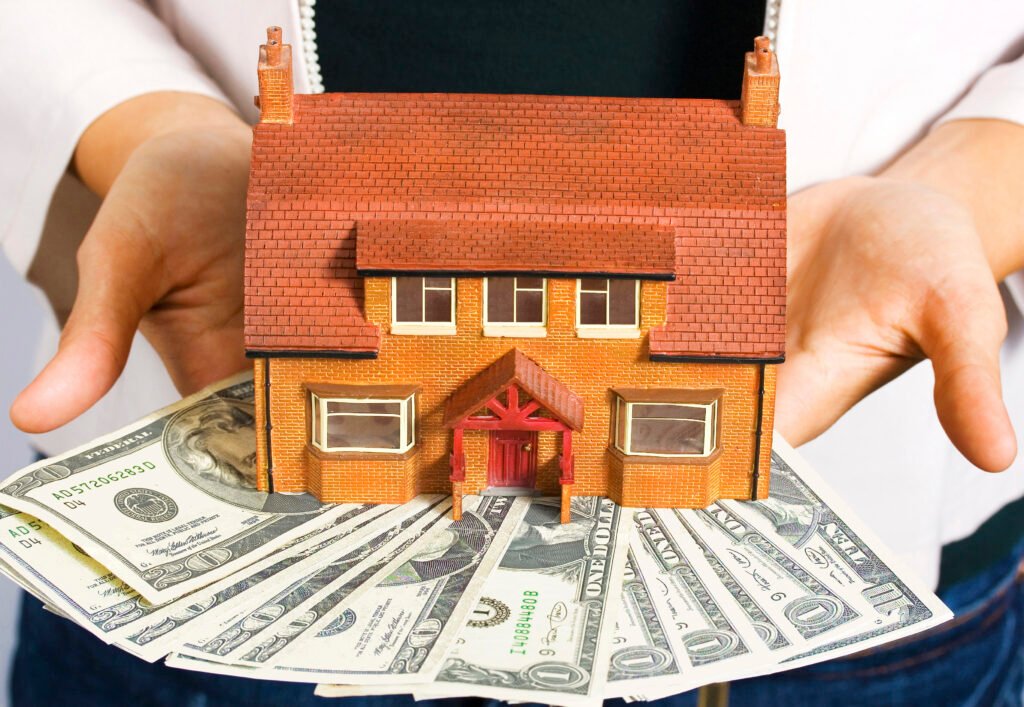 A person holding a miniature house and some dollar bills